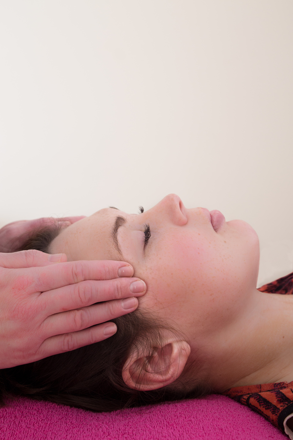 reiki being provided to client lying on massage bed to their head.
