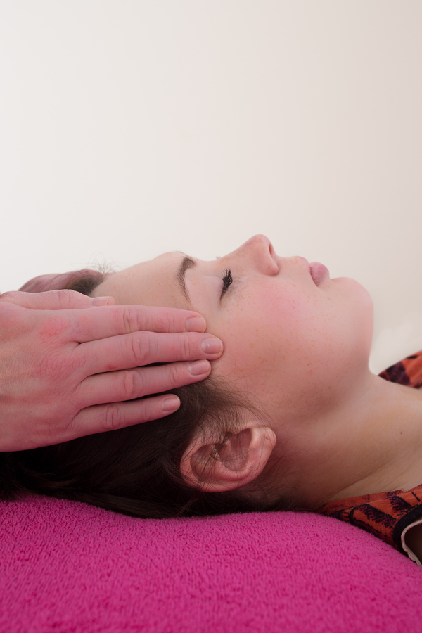 reiki being provided to client lying on massage bed to their head.
